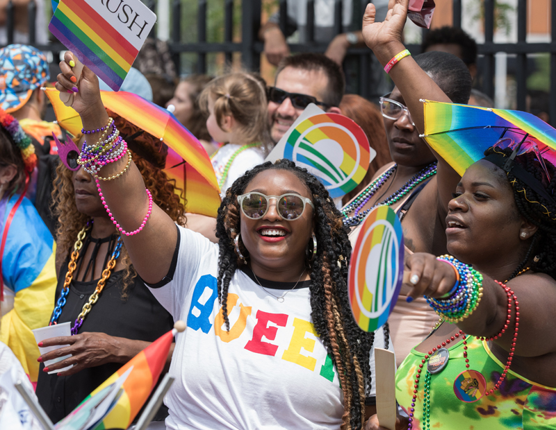 Pride parade attendees cheer with rainbow flags and “QUEER” shirts, celebrating LGBTQ+ pride and inclusion in Chicago’s vibrant Northalsted community